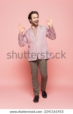 Full length of cheerful host of event showing okay gesture on pink background