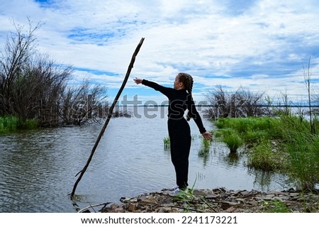 A girl in dark clothes, standing on the seashore. Trains with a stick.