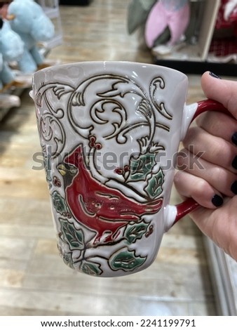 The top down, close up view of a woman holding a coffee mug with a picture of a male cardinal perched in a holly bush.