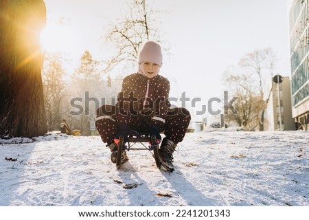 A girl on a sled rides down a hill. Winter. 