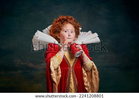 Portrait of little red-headed girl in costume of royal person drinking soda isolated over dark green background. Concept of historical remake, comparison of eras, medieval fashion, emotions, queen Royalty-Free Stock Photo #2241208801
