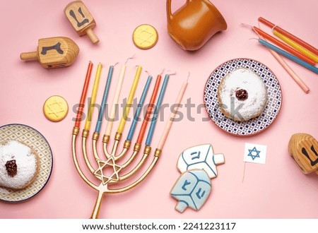 Menorah with treats and dreidels for Hannukah celebration on pink background