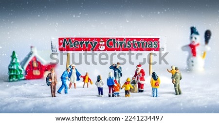 Merry Christmas banner above Santa Claus giving out presents to children and parents in the snow with a house and snowman in the picture.