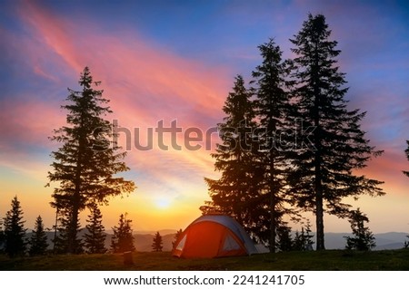 Tent in a clearing in the mountains at a beautiful sunrise.
