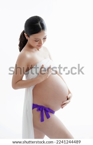 Beautiful Asian Female Expecting Baby, Mom-to-be  Smile and touch Belly  in a Purple  Look at her Belly
