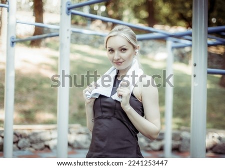 Portrait of cute fit blonde woman with towel on shoulders on sports ground
