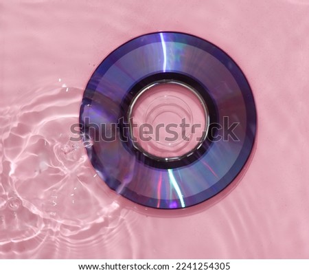 Cd disk in pink water with shadows. Top view