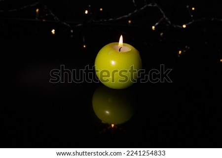Burning round candle on black background with Christmas lights. Christmas time.