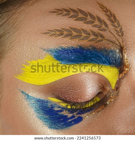 Art makeup on woman eye. Large photo frame. Square composition. Ukrainian flag concept, wheats. Golden field of spikelets on skin, face. Civilians against the war in Ukraine. Stop Russian aggression