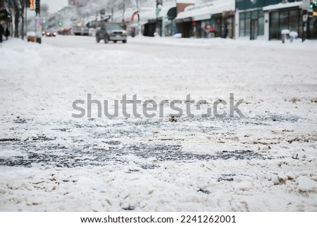 Snow covered city intersection, close up. Low angle view of main road not serviced or plowed with ice and slush. Stay at home and don't travel advice. East Vancouver, BC, Canada. Selective focus.  Royalty-Free Stock Photo #2241262001