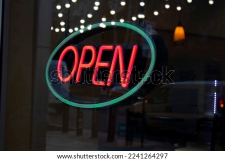 Neon sign on the glass door of the store. Open store. Shop. Word in oval shape. Red and green. The concept of the restaurant, bar. Night lights and garlands