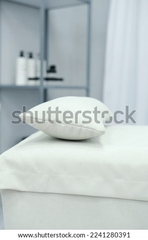 The interior of the office of a massage specialist. A white couch with a pillow stands against the background of a shelf with cosmetics. Vertical photo