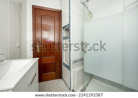 Bathroom with a small white porcelain sink with a shower cabin with translucent glass sliding doors and a mahogany door
