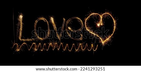 Inscription Love and heart of sparklers. Sparks of holiday lights on black background with heart and spiral