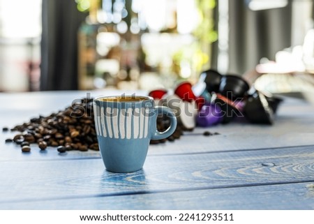Coffee still life with a blue porcelain cup with assorted capsules and blurred coffee beans on a blue wooden plank table