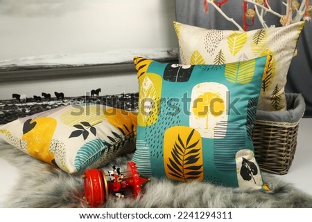Three different patterned colored throw pillows on the shaggy carpet stand next to a photograph, basket and toy in the living room.
