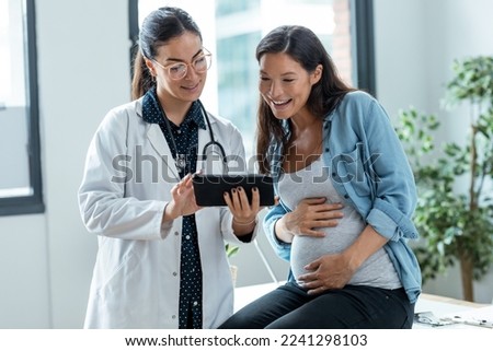 Shot of female gynecologist doctor showing to pregnant woman ultrasound scan baby with digital tablet in medical consultation. Royalty-Free Stock Photo #2241298103