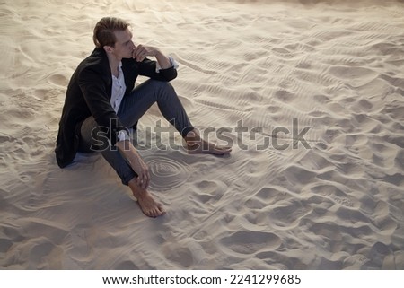 sad financier is frustrated, a young man with big plans is faced with a global economic crisis, concept. businessman in a suit is sitting on a pile of sand