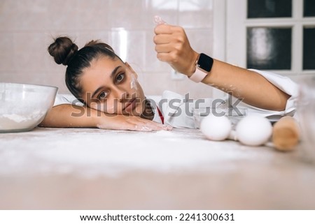 Tired young woman is pouring flour on the kitchen table
