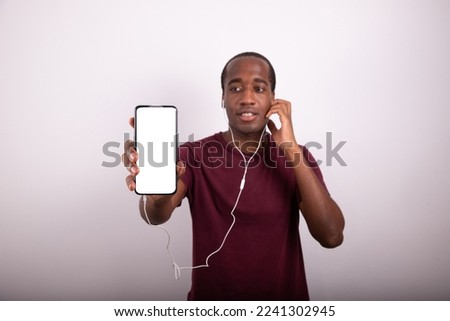 A man listens to an audio with earphones showing the screen of his smartphone, blank screen with mockup, advertising photo