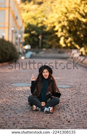 Young woman sitting at city show finger up, new idea