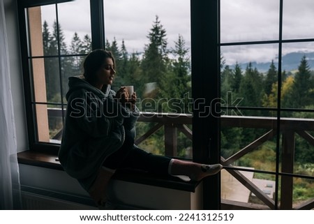 Silhouette of a woman sitting on the windowsill with a mug