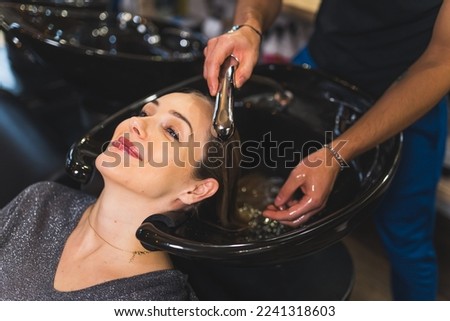 Cropped shot of unrecognizable hairdresser washing blond hair of his positive smiling female client in beauty salon. High quality photo
