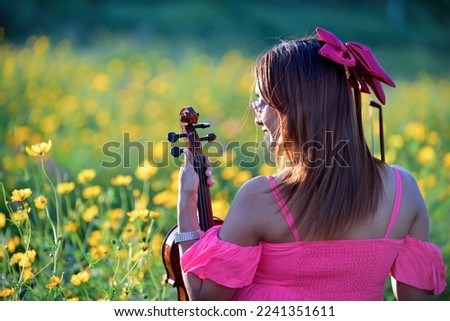 Asian girl playing the violin In a field of blooming flowers, enjoy playing music in a beautiful natural setting.