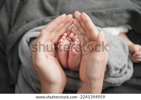 Two legs of a newborn baby in the arms of the mother, on the little fingers of the wedding rings of the parents, selective focus Royalty-Free Stock Photo #2241394959