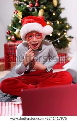 Boy having fun with wear paper glasses holidays decor using online communitation by laptop. Distance Christmas party. Social distancing