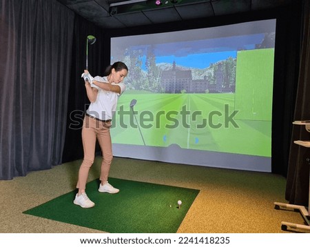 Girl playing golf on screen and golf simulator. Young golfer playing golf video game indoors Royalty-Free Stock Photo #2241418235