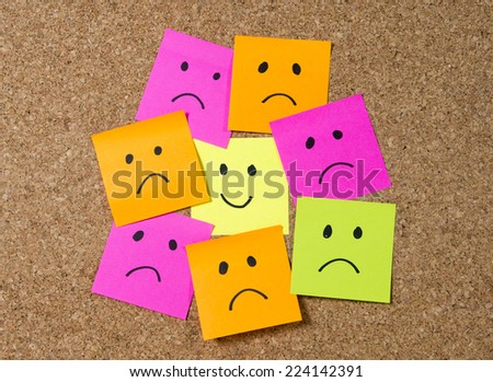 Cartoon face expression on note surrounded by sad and depressed faces on cork message board in happiness versus depression and smile against adversity concept