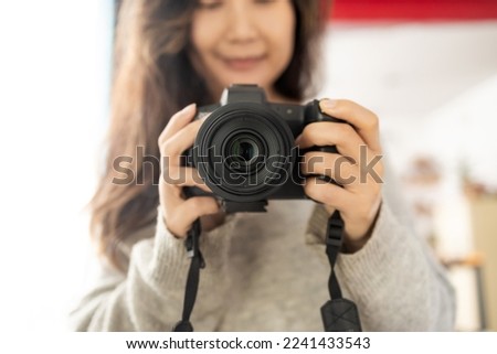 Young female photographer with a camera on a soft background taking pictures with her new camera