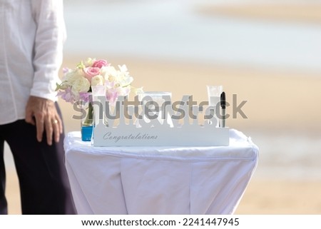 A white congratulatory sign at the wedding, the text that says Mr, Mrs, is placed on the table. along with a bouquet of flowers and a pen located on the beach