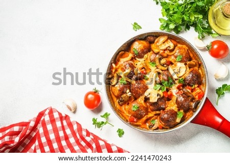 Meatballs with mushrooms in tomato sauce in a frying pan at light stone table. Top view with copy space. Royalty-Free Stock Photo #2241470243
