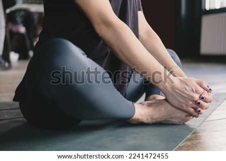 Close-up photo of the legs and torso of a female yogi meditating barefoot and wearing leggings in cobbler's pose (Baddha Konasana) on a yoga mat on the floor