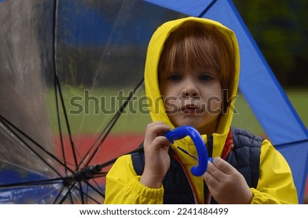 Cute boy preschooler in a yellow raincoat with an umbrella. A child plays outside in the rain. Concept Autumn or fun walks, bad weather, weather forecast, good mood on a cloudy day
