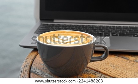 Cup of delicious coffee and laptop on wooden table, closeup