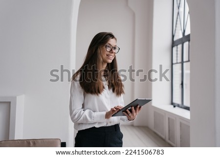 Beautiful young businesswoman using laptop dressed in white shirt and black pants, makes video call smiling wide. Beautiful student girl having remote lesson. Successful entrepreneur female at office.