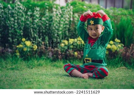 Cute Asian boy in elf's costume in green nature garden outdoor background with space for text 
Make a Big Heart
