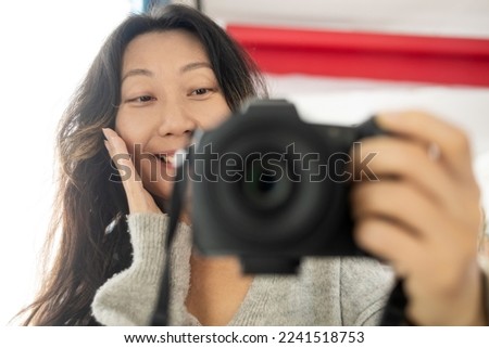 Enthusiastic cheerful photographer holding a dslr camera in her home office. Female photographer smiling cheerfully while working at her desk. Creative female freelancer working on a new project.