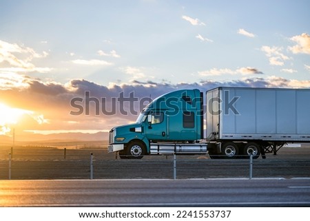 Industrial long hauler big rig green semi truck tractor with chrome parts transporting commercial cargo in loaded dry van semi trailer running on the highway road at sunset time in California Royalty-Free Stock Photo #2241553737