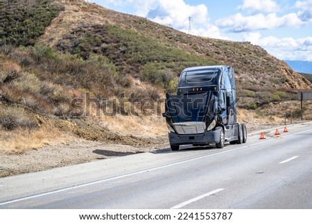 Broken big rig semi truck tractor with open hood and accident warning emergency signs standing on the road shoulder waiting for towing truck for the diagnostic technician inspection and quick repair