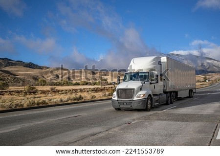 Industrial long hauler big rig white semi truck tractor with chrome parts transporting commercial cargo in loaded dry van semi trailer running on the highway road at sunny day in California Royalty-Free Stock Photo #2241553789