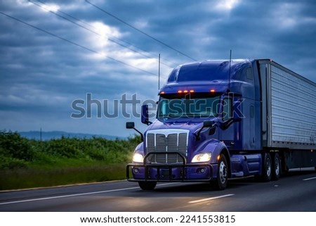 Blue industrial long haul Big rig semi truck with high cab transporting frozen commercial cargo in refrigerator semi trailer running on the evening wide highway road with storm clouds in Oregon Royalty-Free Stock Photo #2241553815