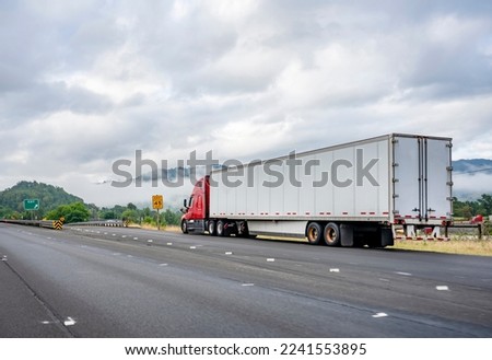Bright red industrial long haul big rig semi truck with dry van semi trailer stands on the side of the road having made a planned stop for a break according to schedule of movement along the log book Royalty-Free Stock Photo #2241553895