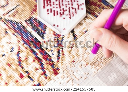 A woman collects a diamond mosaic.The process of creating a picture of multicolored rhinestones. Diamond mosaic painting fragment of making close-up top view, handmade hobby.