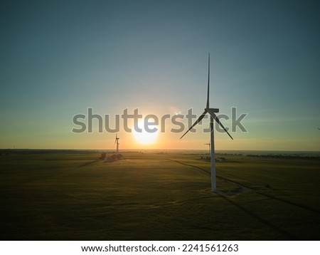 Aerial wide view of a silhouette many wind turbine standing in a wheat field at sunset. Wide shot