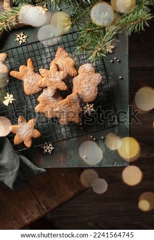 Christmas cookies or gingerbreads of various shapes on pastry cooling rack on green wooden table. Xmas or new year composition with fir tree and bokeh lights, top view, flat lay