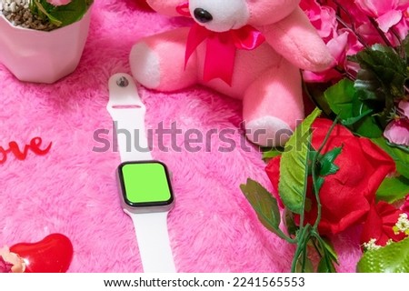 Green screen mockup of a smartwatch, surrounded by dolls and flower, and a pink fluffy carpet as the background